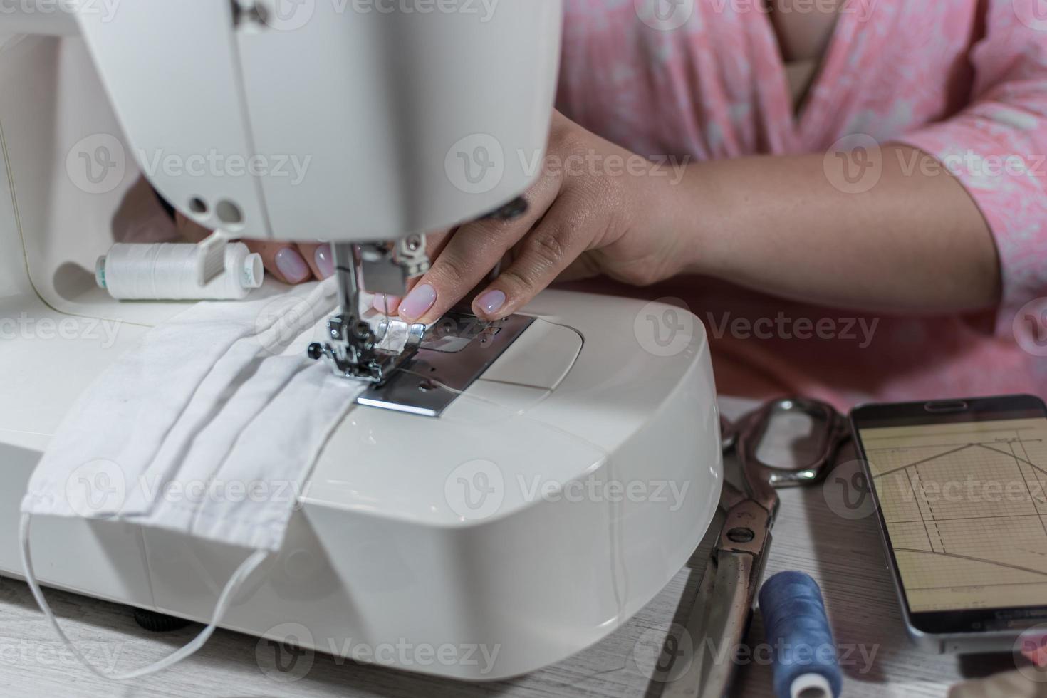 mujer cose una máscara médica en la cara en una máquina de coser en el marco de las manos visibles. foto