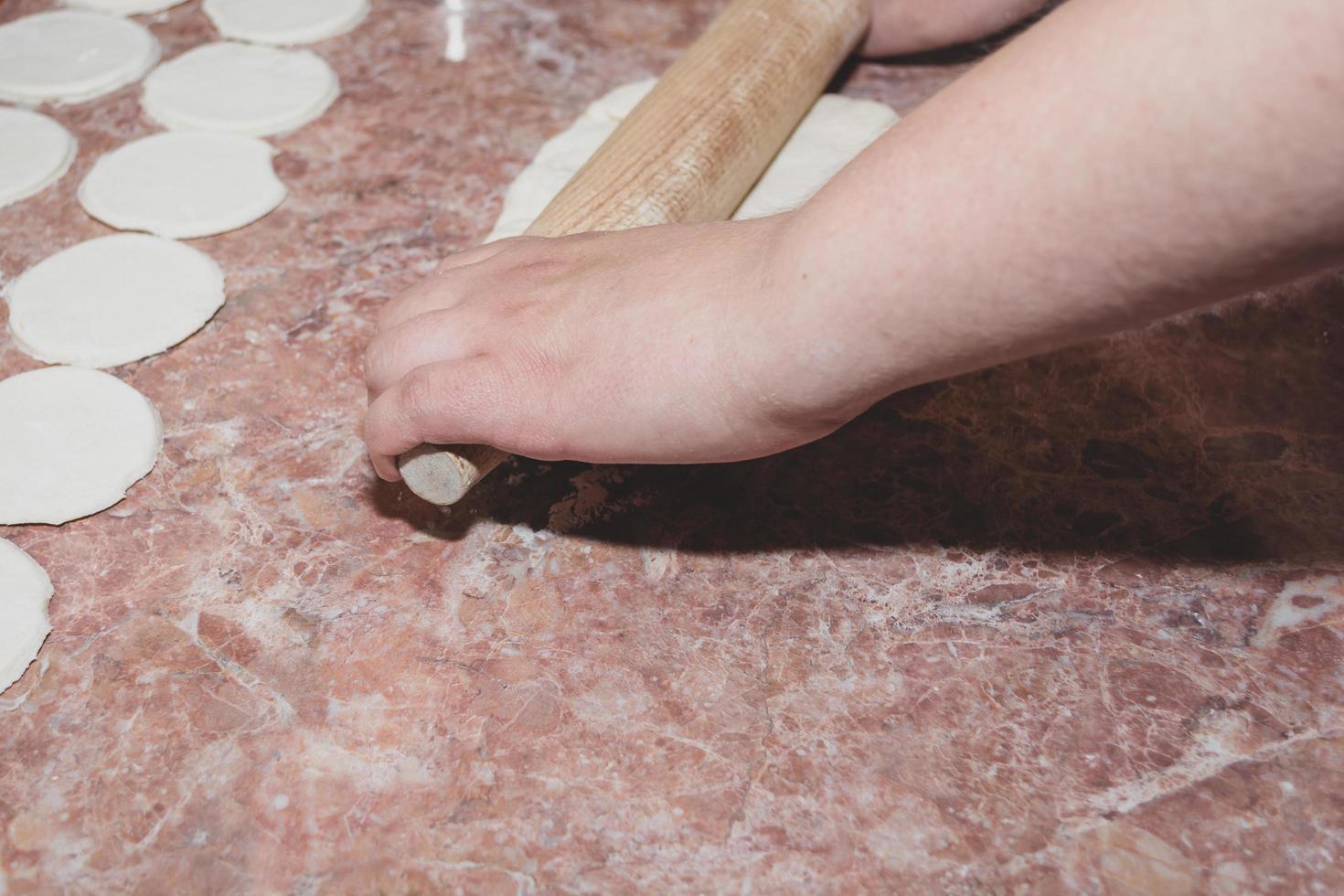 A woman rolls out the dough with a wooden rolling pin on a marble kitchen countertop. photo