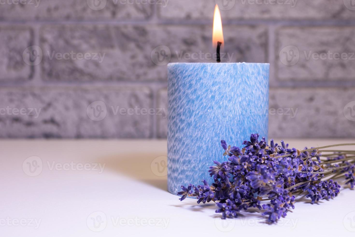 Dry bouquet of lavender flowers near a burning blue candle on the background of a blurred brick wall in the interior. photo