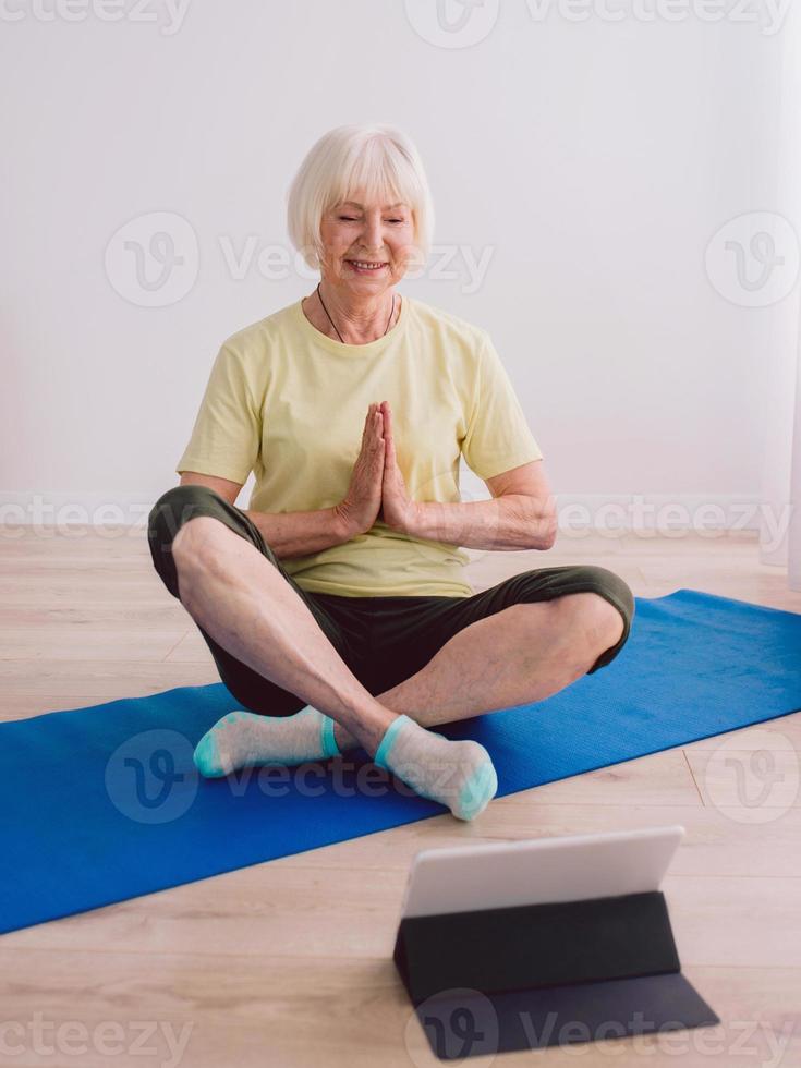 senior woman doing yoga online indoor. Anti age, sport, technology, yoga concept photo