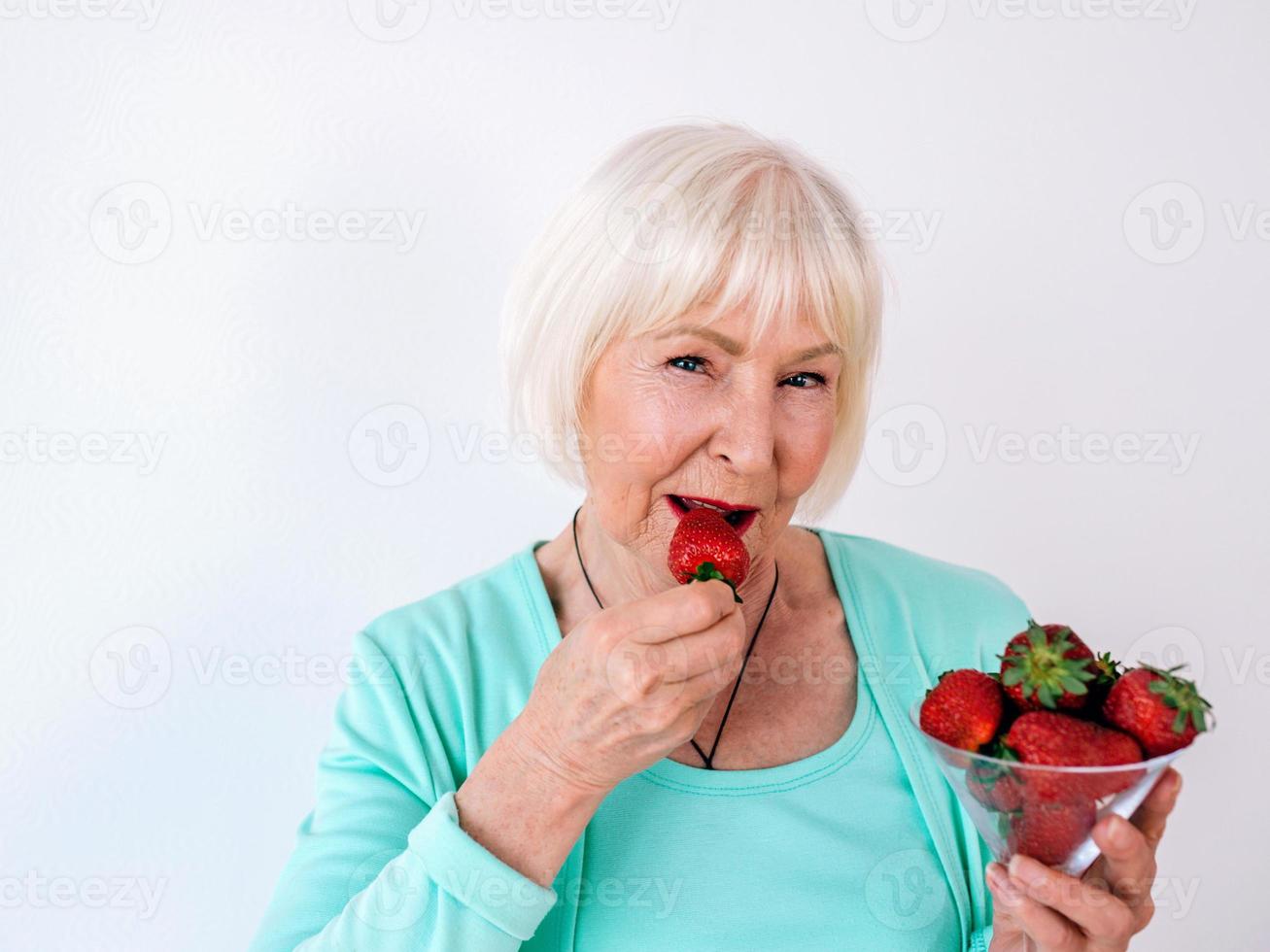 Retrato de mujer alegre con estilo senior en ropa turquesa comiendo fresas. verano, viajes, anti edad, alegría, jubilación, fresas, bayas, vitaminas, concepto de libertad foto