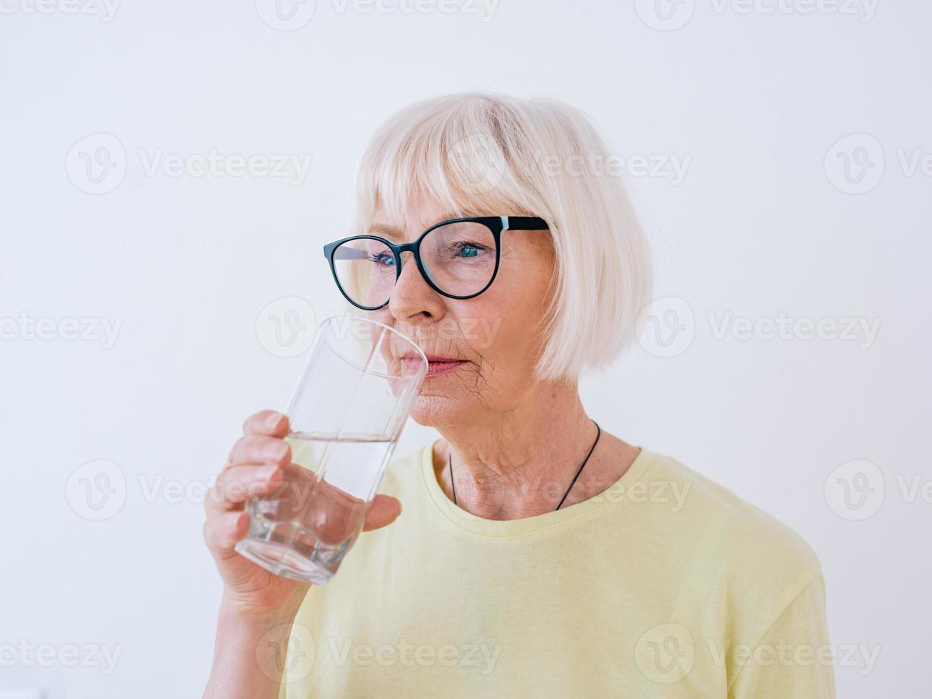 mujer mayor sosteniendo un vaso de agua y agua potable. estilo de vida saludable, deporte, concepto anti-edad foto