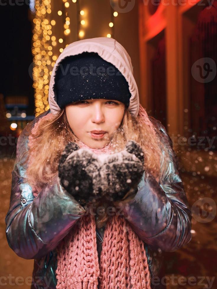 Happy smiling young Caucasian woman in scarf, hat, jacket, mittens at winter night outdoor. New year, fun, winter concept photo