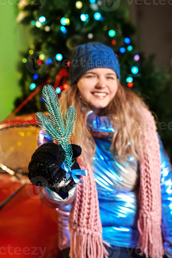 Happy smiling young Caucasian woman in scarf, hat, jacket, mittens by the christmas tree outdoor. New year, fun, winter concept photo
