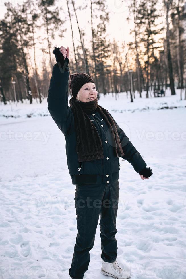 mujer mayor con sombrero y chaqueta deportiva haciendo ejercicios deportivos en el parque de invierno de nieve. invierno, edad, deporte, actividad, concepto de temporada foto