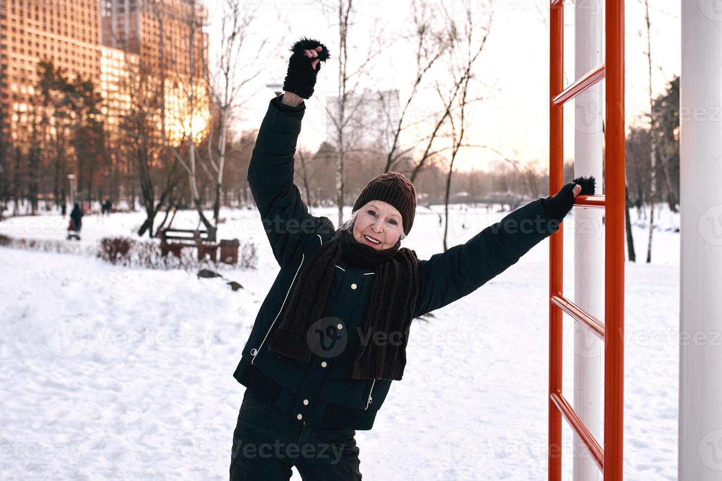 mujer mayor con sombrero y chaqueta deportiva haciendo ejercicios deportivos en el parque de invierno de nieve. invierno, edad, deporte, actividad, concepto de temporada foto