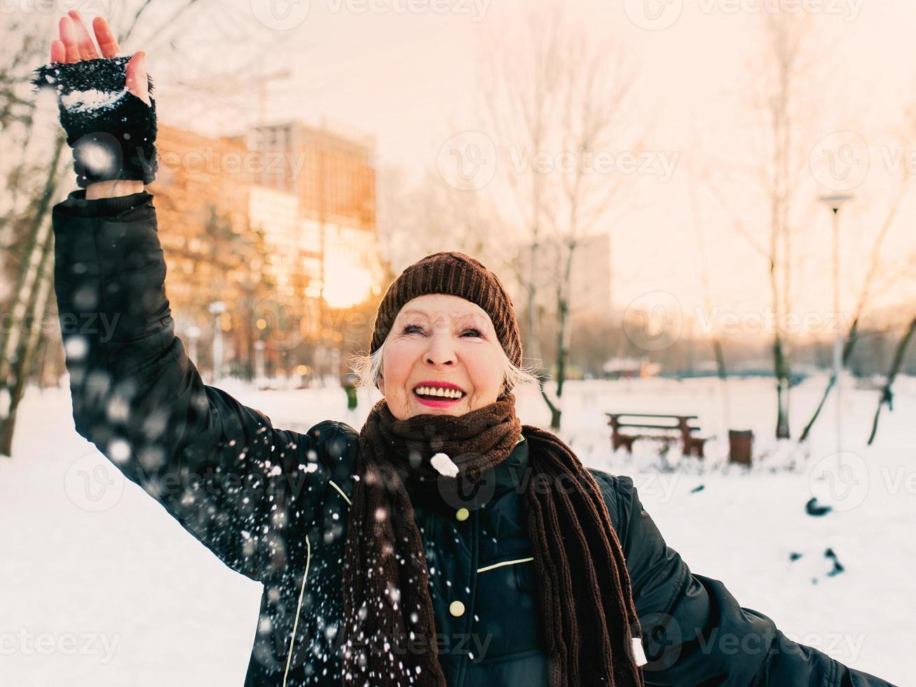 mujer mayor con sombrero y chaqueta deportiva bolas de nieve en el parque de invierno de nieve. invierno, edad, deporte, actividad, concepto de temporada foto