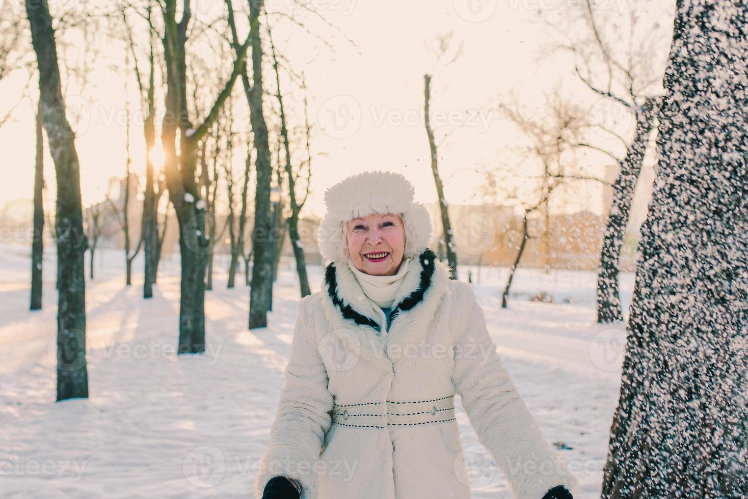 mujer mayor con sombrero blanco y abrigo de piel con nieve en las manos en el bosque de nieve. invierno, edad, concepto de temporada. foto