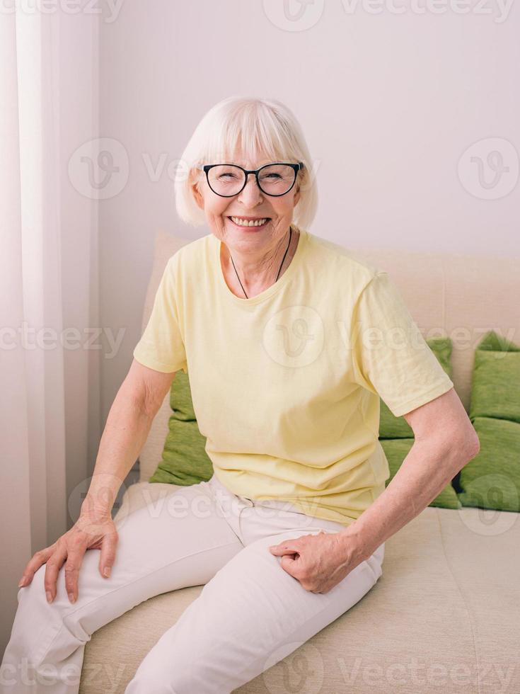 cheerful caucasian stylish woman with gray hair sitting on the couch at home. Anti age, healthy lifestyle, positive thinking concept photo