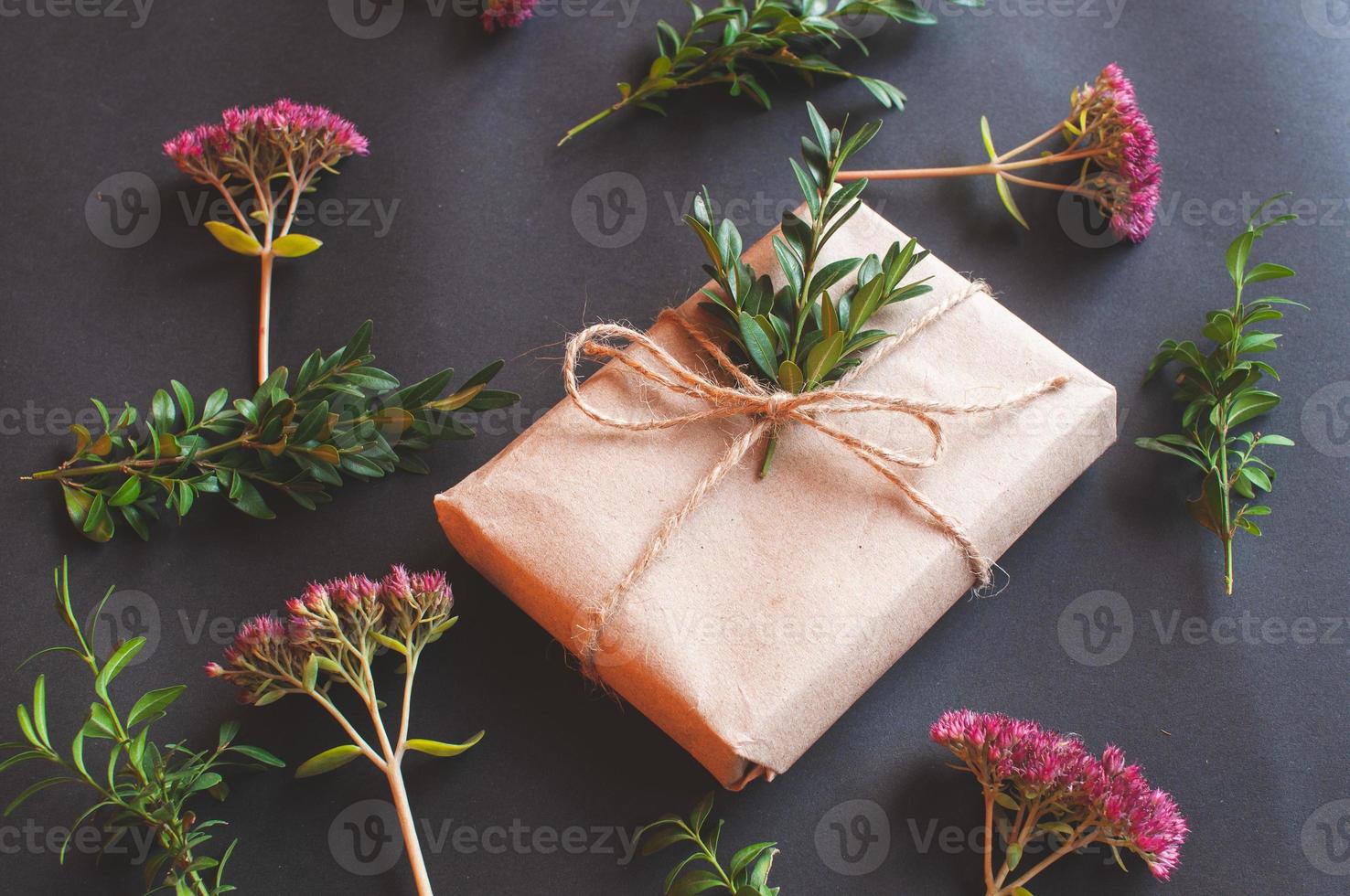 Caja de regalo artesanal con nudo natural con florecitas rosadas sobre fondo negro foto