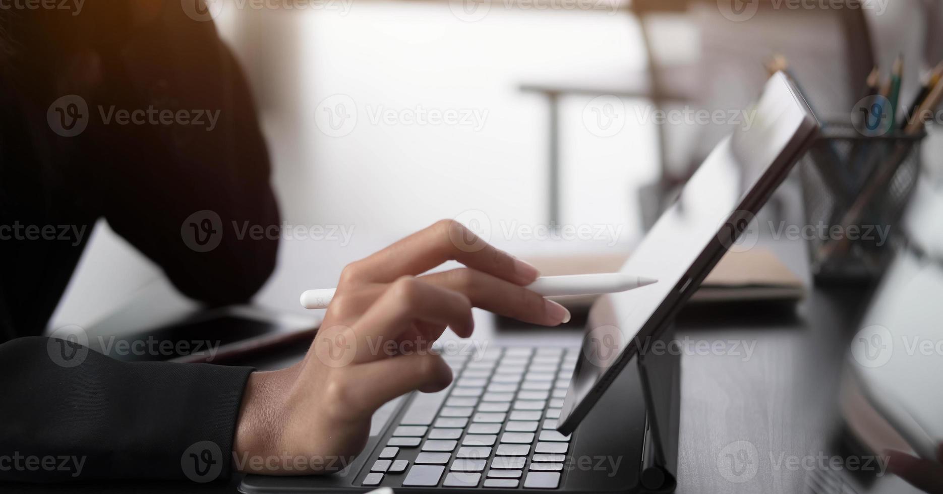 Cerrar la mano de la mujer con lápiz óptico escribiendo en el bloc de notas digital, tocando en la pantalla de la tableta digital trabajando en una computadora portátil en la oficina. diseñador web trabajando en su proyecto. foto