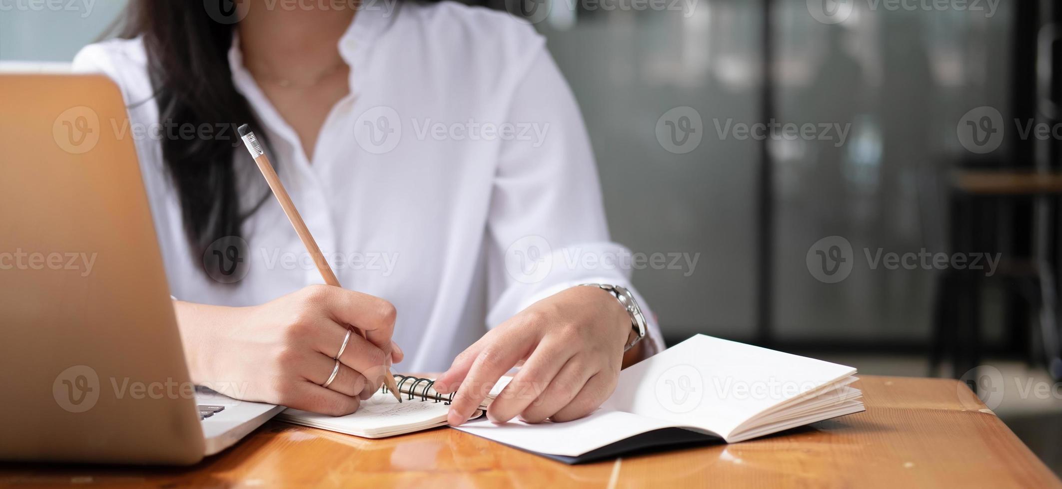 Cropped photo hand of woman writing making list taking notes in notepad working or learning online with laptop at home