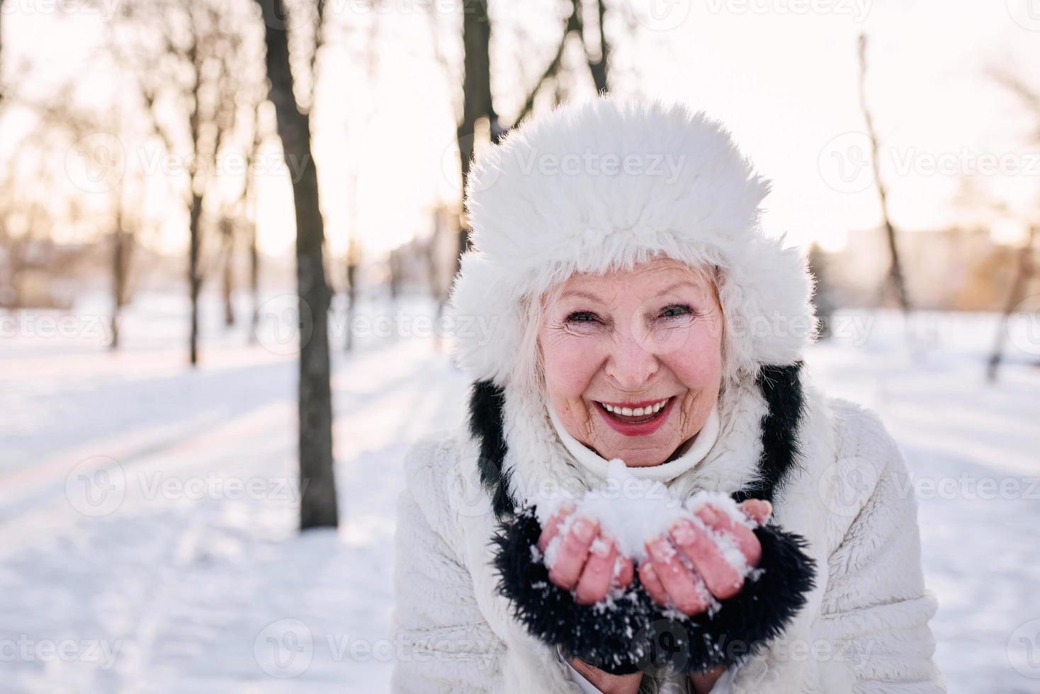 mujer mayor con sombrero blanco y abrigo de piel disfrutando del invierno en el bosque nevado. invierno, edad, concepto de temporada. foto