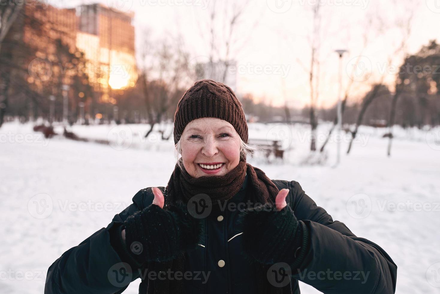 senior woman in hat and sporty jacket doing sports exercises in snow winter park. Winter, age, sport, activity, season concept photo