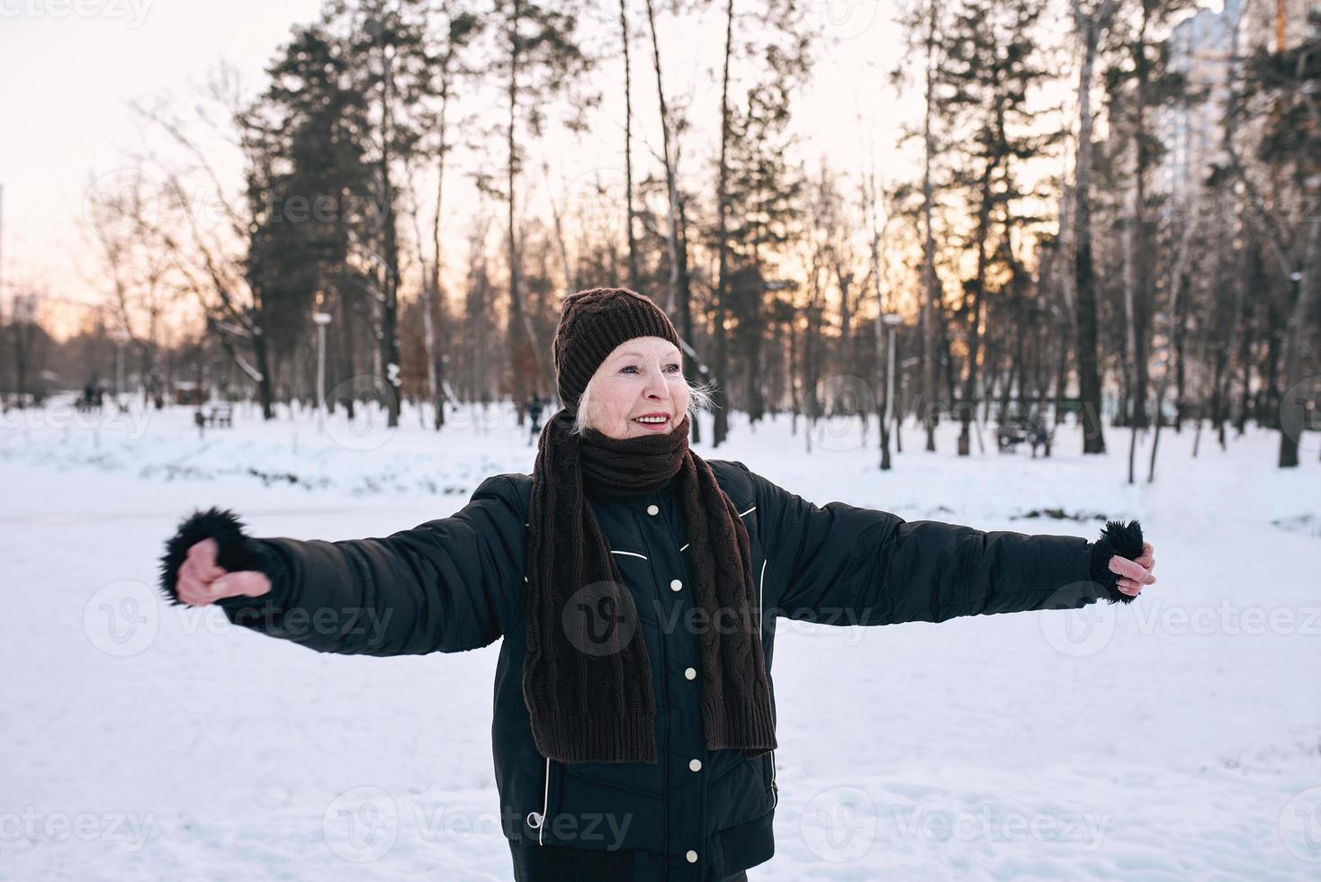 senior woman in hat and sporty jacket doing sports exercises in snow winter park. Winter, age, sport, activity, season concept photo