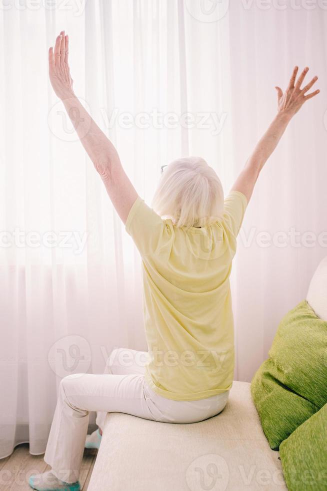 alegre mujer caucásica con estilo con el pelo gris sentado en el sofá en casa. anti edad, estilo de vida saludable, concepto de pensamiento positivo foto