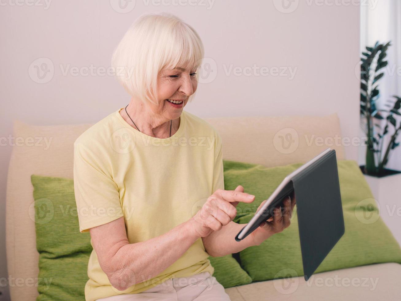 mujer elegante caucásica alegre senior con cabello gris con su tableta en casa. tecnología, emociones, familia, estilo de vida saludable, concepto de pensamiento positivo foto