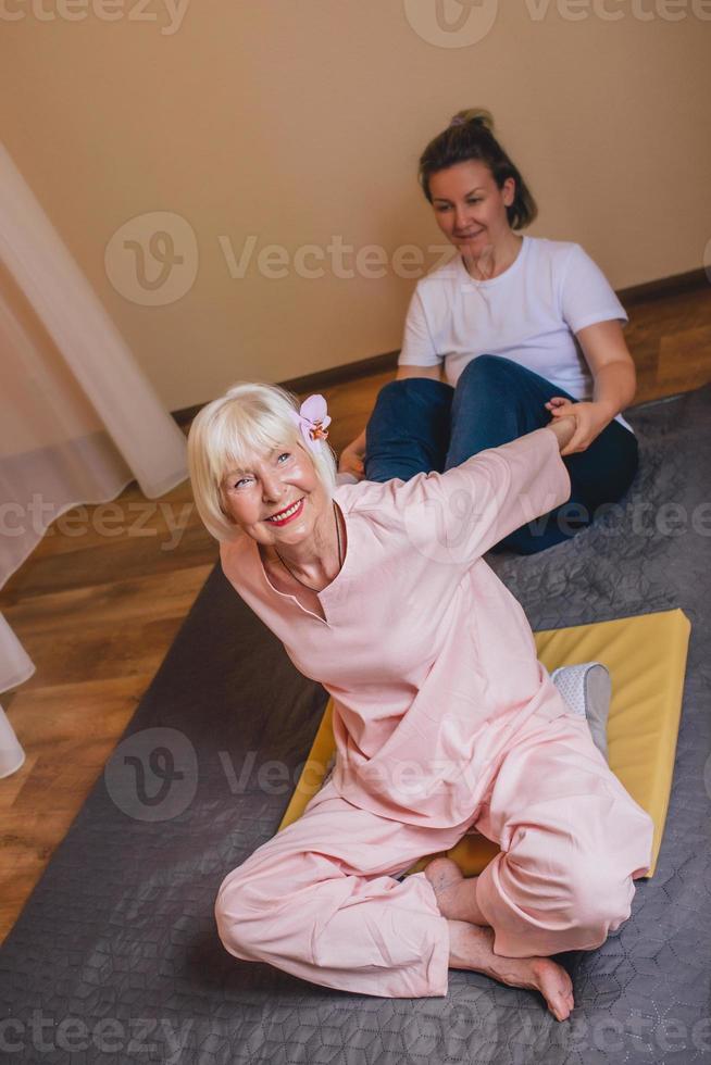 Senior mujer elegante caucásica con cabello gris y phalaenopsis rosa en su cabello sentado en masaje tailandés. anti edad, estilo de vida saludable, viajes, concepto de masaje tailandés foto