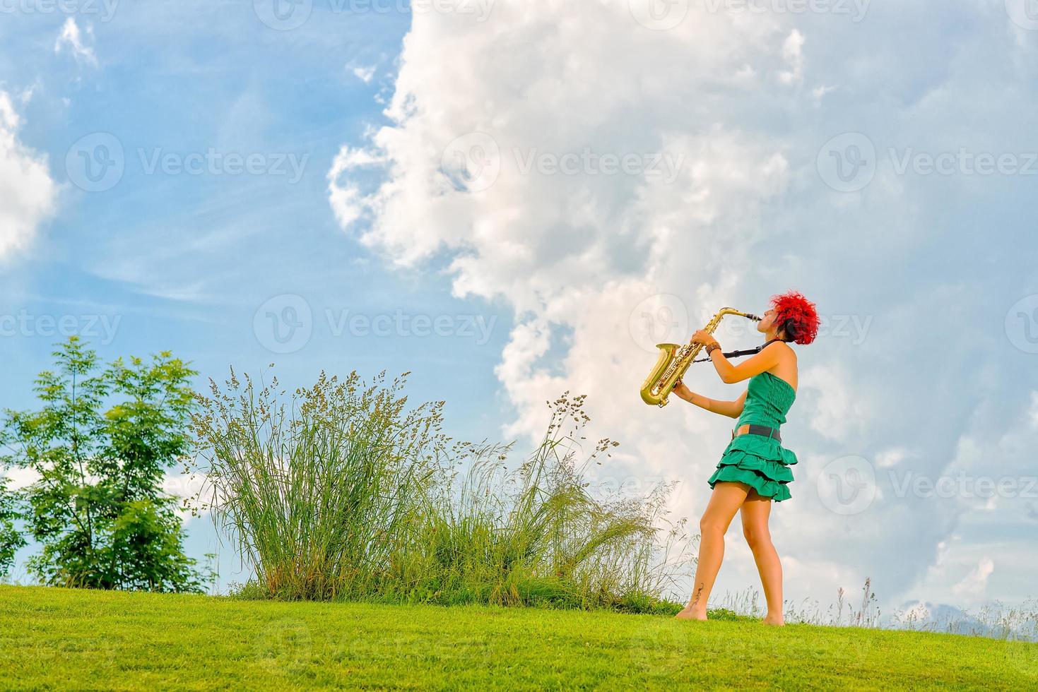 Young saxophonist woman with the red hair playing saxophone in the mountain nature. photo