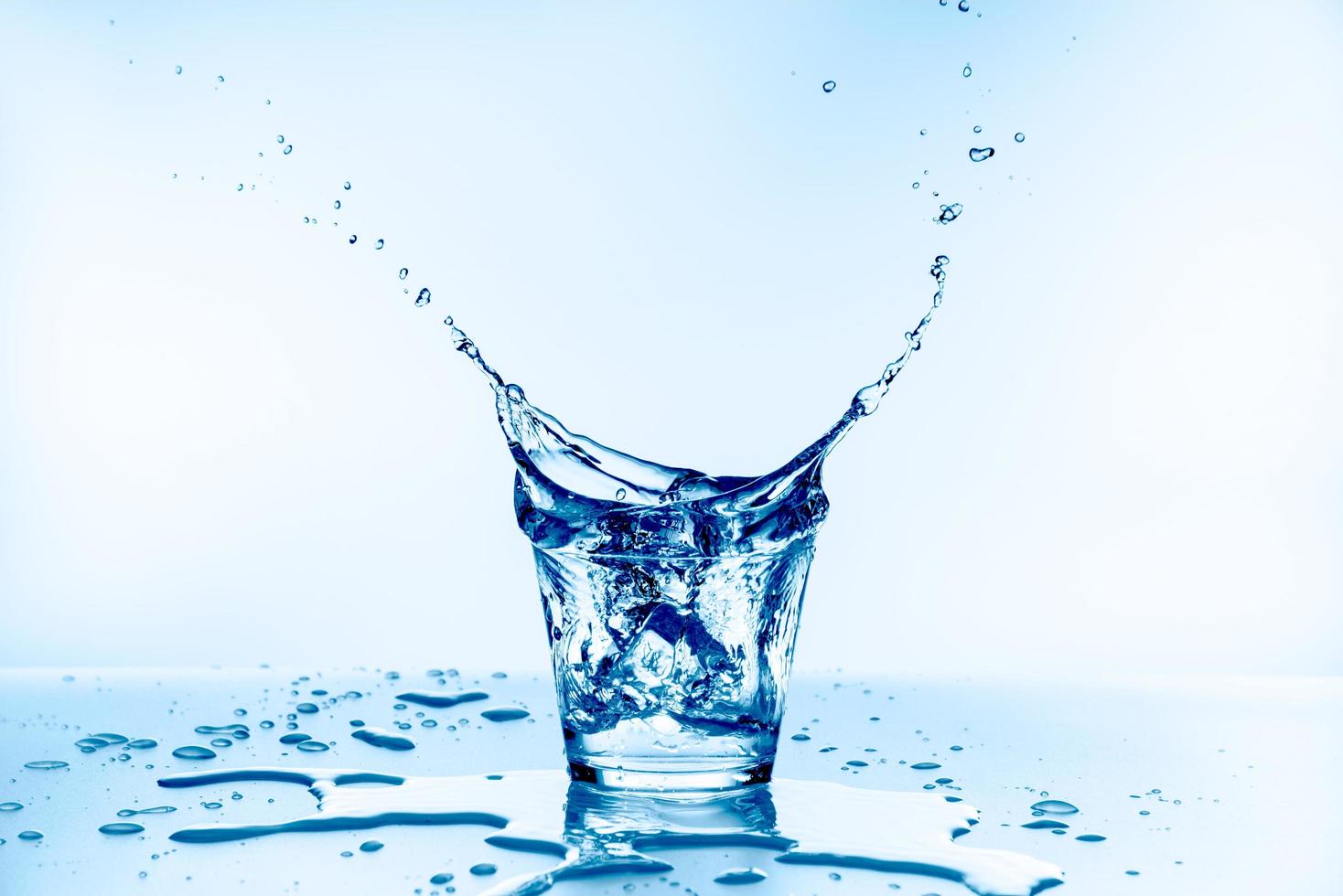 Hielo que cayó en el vaso con salpicaduras de agua de vidrio aislado sobre fondo azul. foto