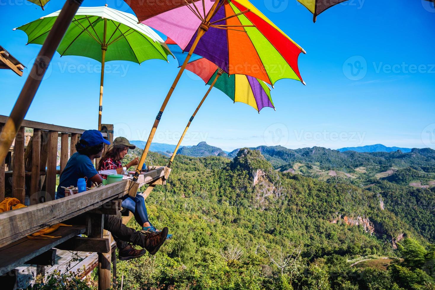 Pareja de turistas asiáticos sentados comen fideos en la plataforma de madera y mirando la vista panorámica de la hermosa naturaleza de las montañas en ban jabo, mae hong son, thialand. foto