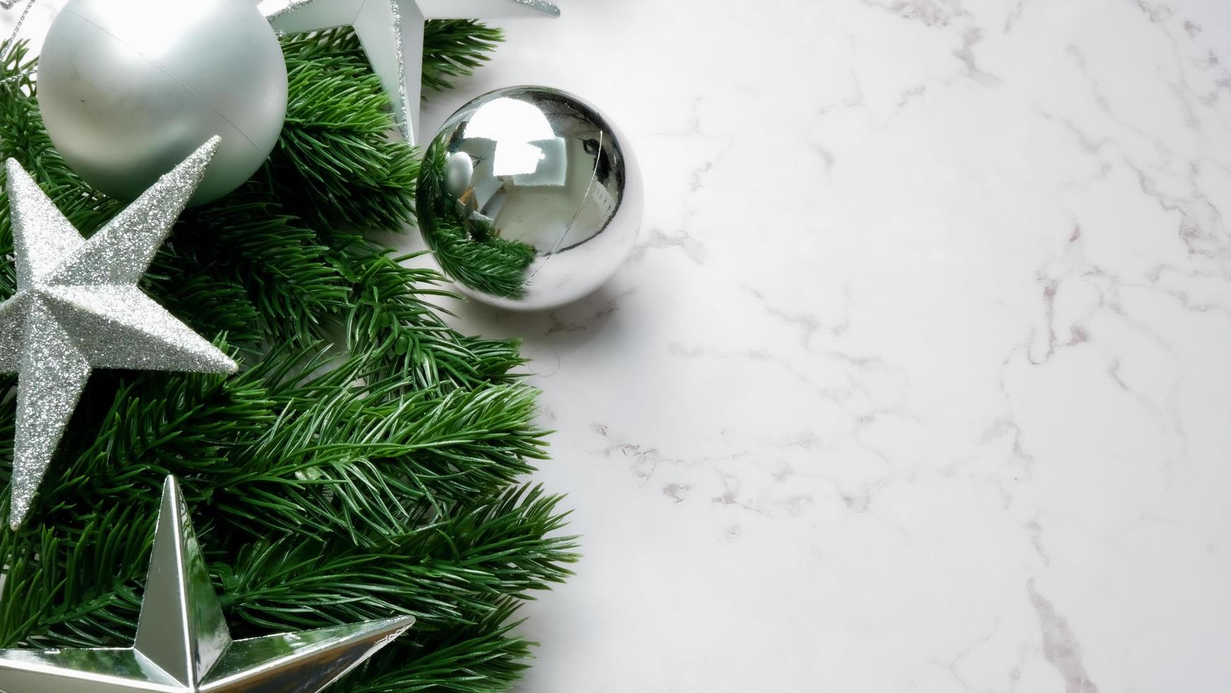 Green pine tree leaves on white marble background, christmas decorations in bright silver color. Simple and creative christmas concept. photo