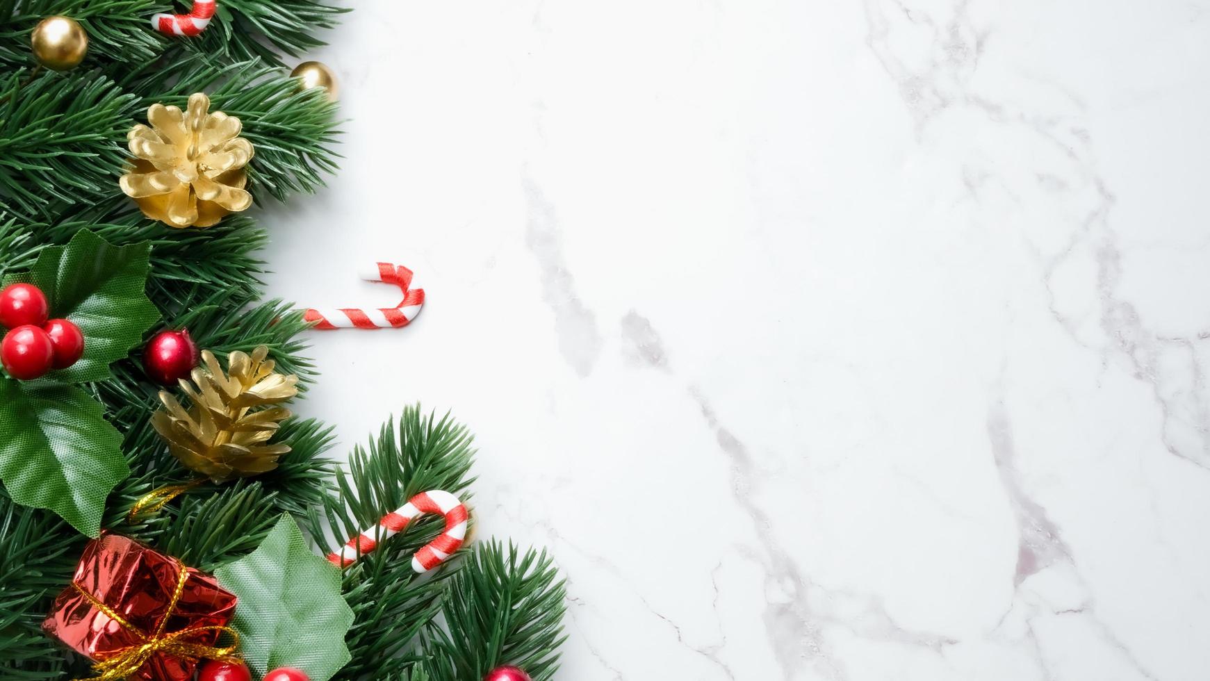 Green pine tree leaves, red christmas decorations and candy canes on white marble background, christmas decorations in bright red color. Simple and creative christmas concept. photo