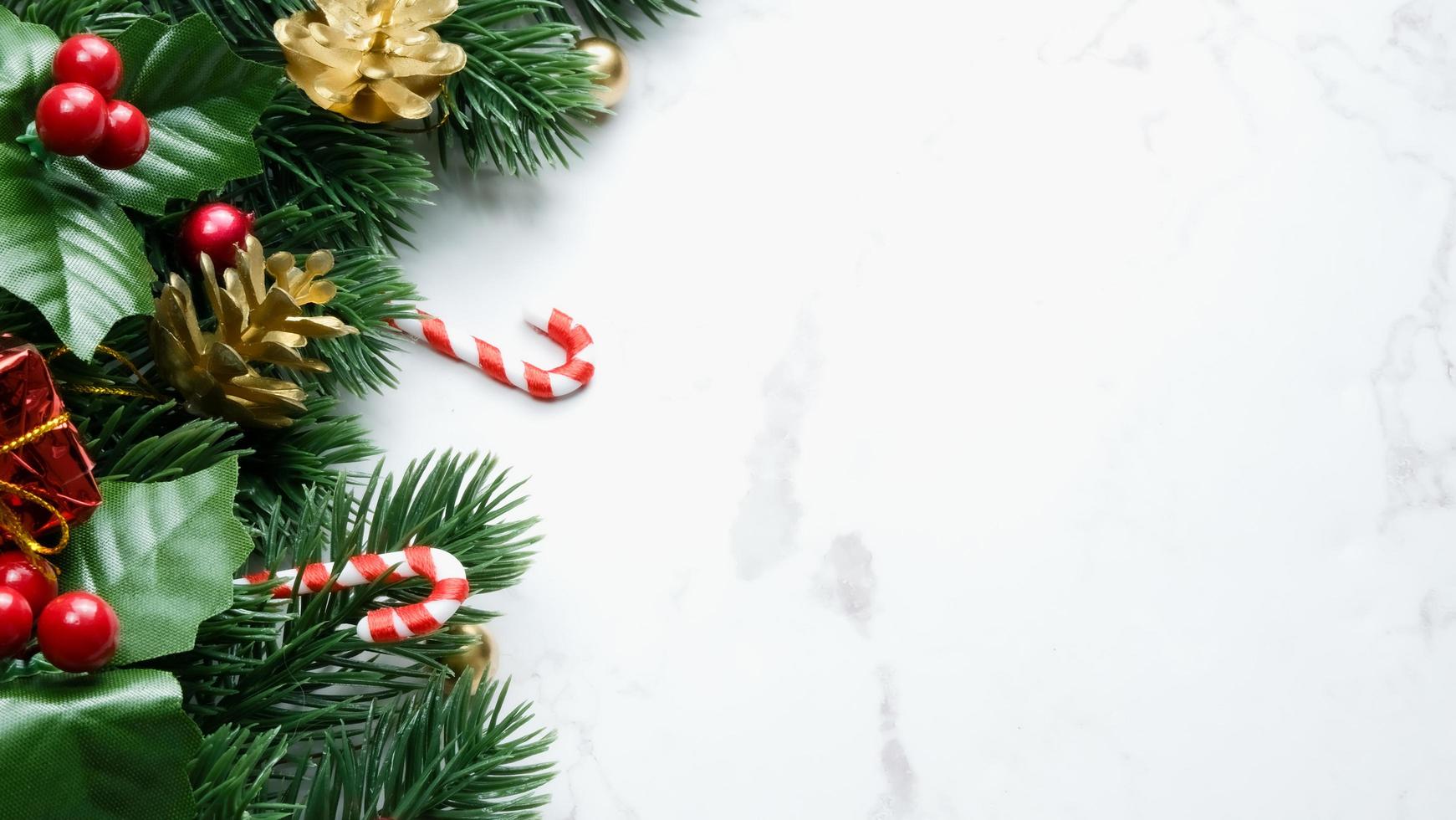 Green pine tree leaves, red christmas decorations and candy canes on white marble background, christmas decorations in bright red color. Simple and creative christmas concept. photo