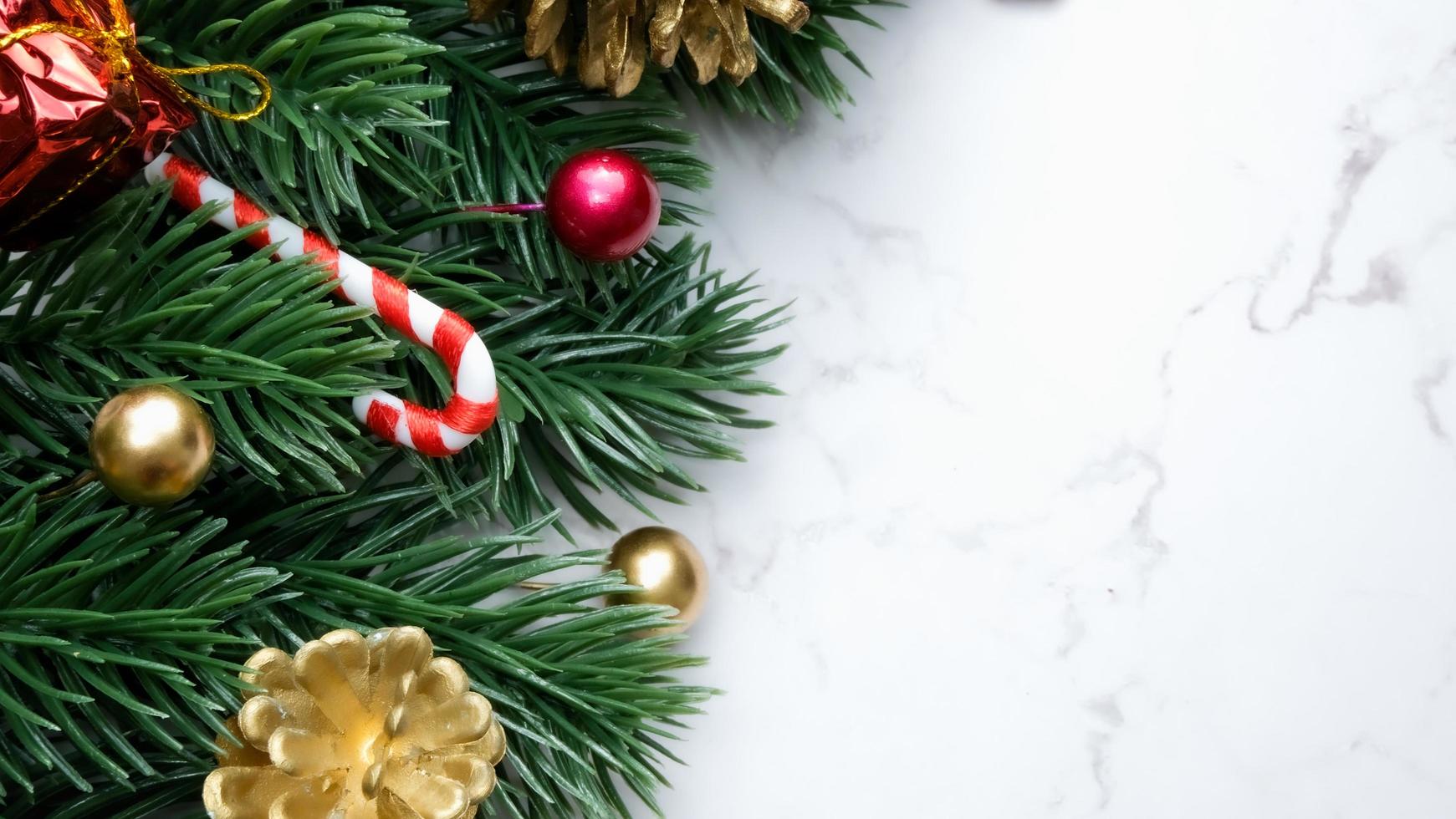 hojas de pino verde, adornos navideños rojos y bastones de caramelo sobre fondo de mármol blanco, adornos navideños en color rojo brillante. concepto de navidad simple y creativo. foto