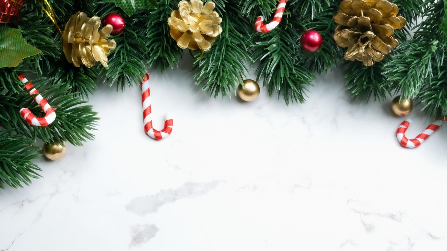 hojas de pino verde, adornos navideños rojos y bastones de caramelo sobre fondo de mármol blanco, adornos navideños en color rojo brillante. concepto de navidad simple y creativo. foto