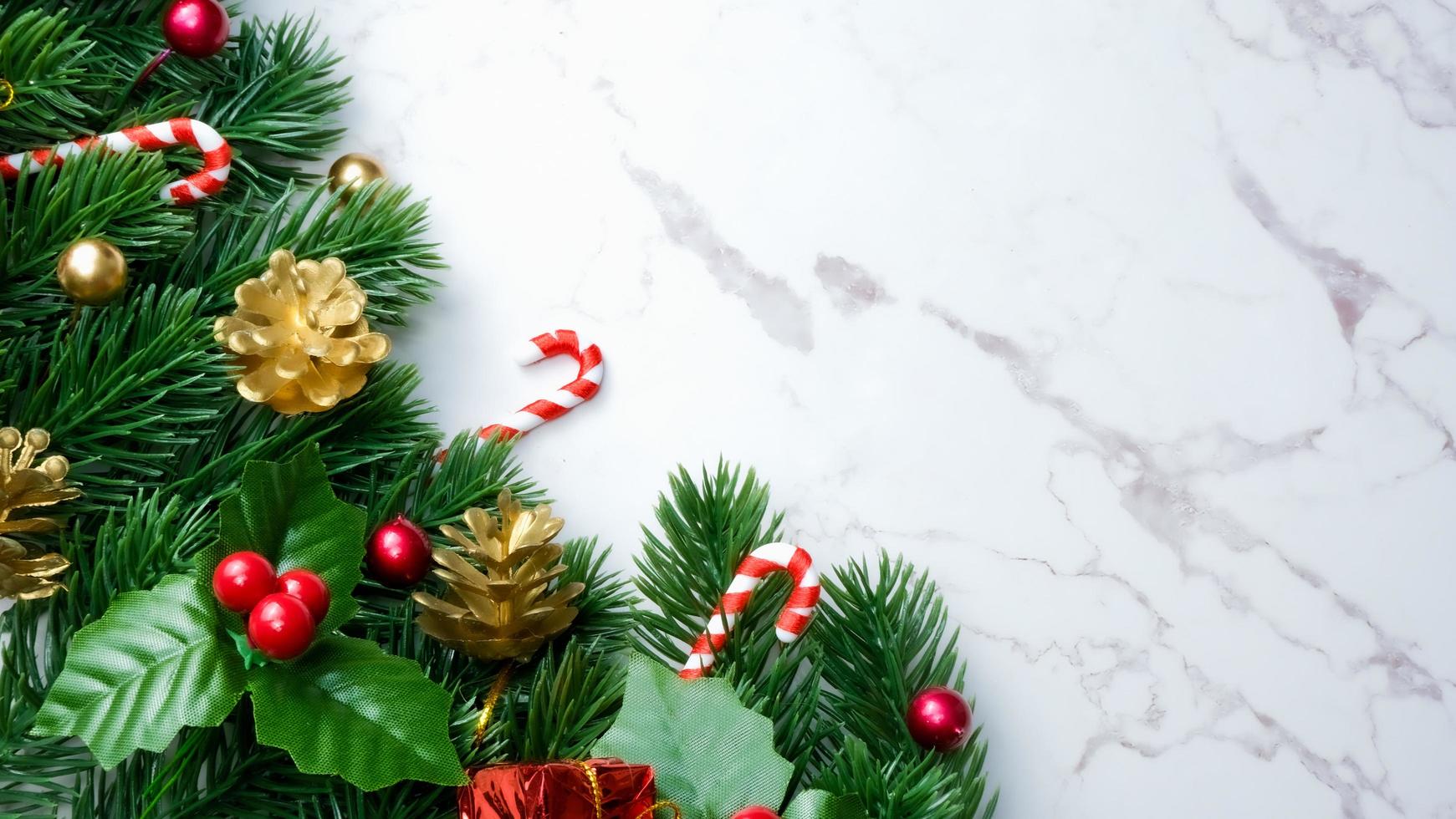 Green pine tree leaves, red christmas decorations and candy canes on white marble background, christmas decorations in bright red color. Simple and creative christmas concept. photo