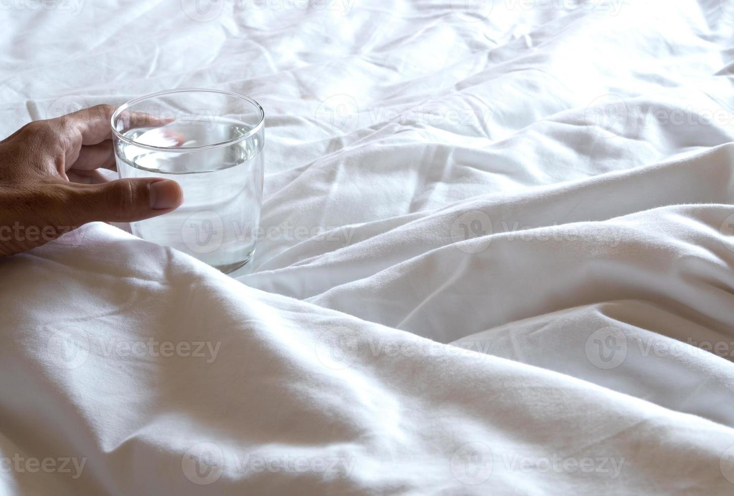 mano sosteniendo el vaso de agua en la cama foto