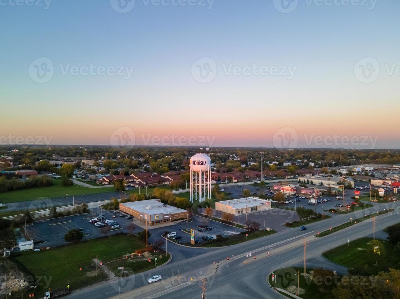 aerial view of urban area with water tower prominent in city wide highway large industrial area with parking lot single-family homes in background sun starting to set photo