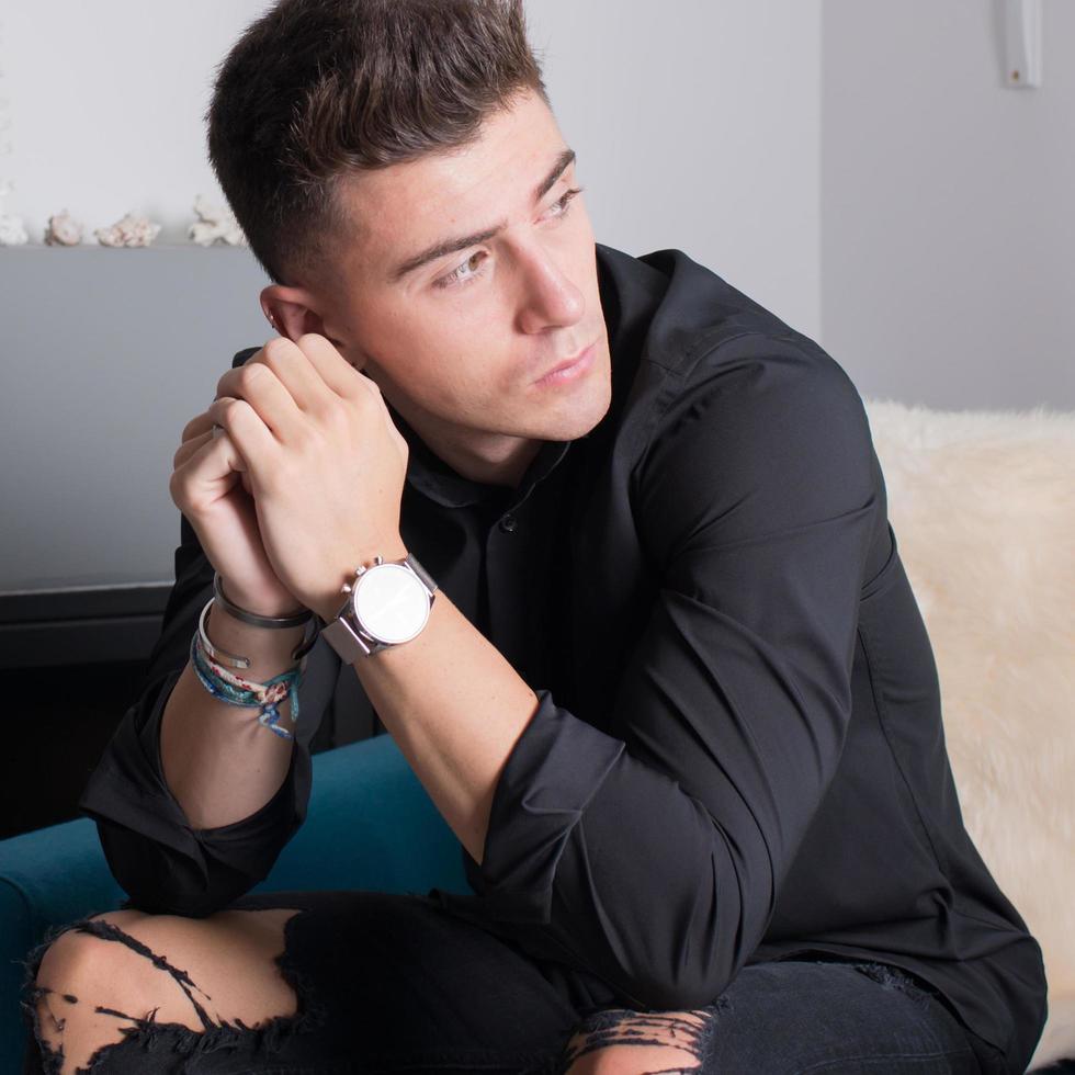 Close up of an attractive young man sitting in a modern living room looking to his left. photo