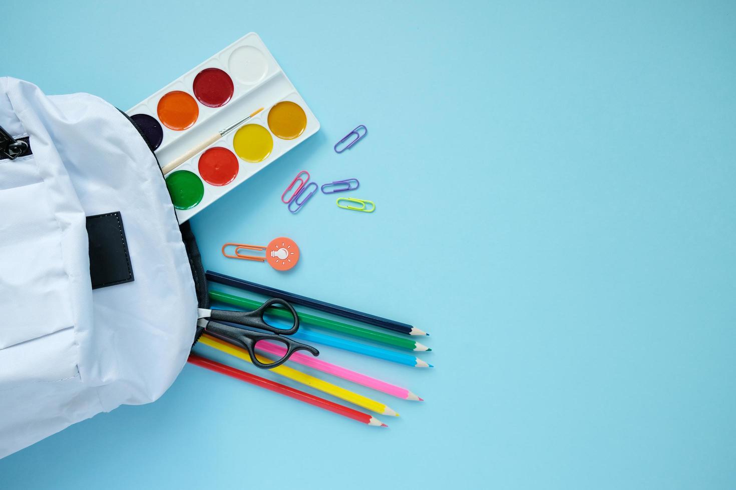 Backpack with different colorful stationery on table. photo