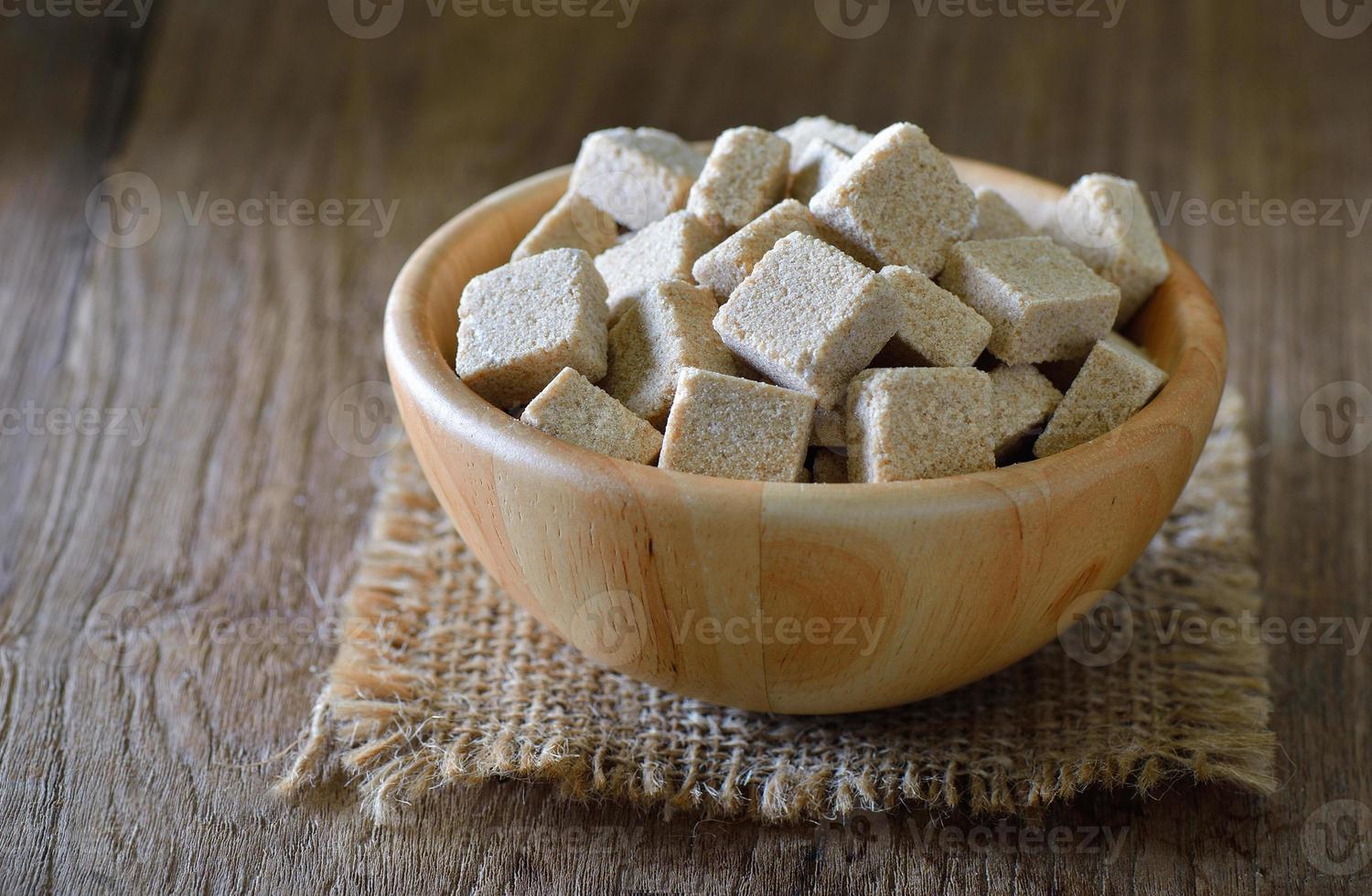 Terrones de azúcar en un tazón de madera sobre la mesa de madera foto