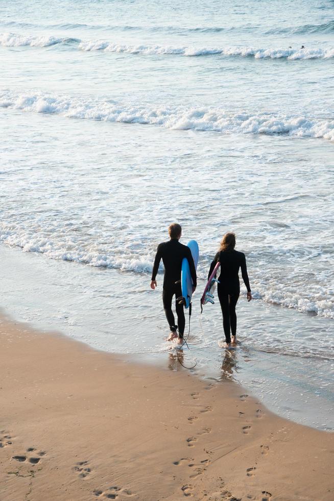 Youn couple wearing wetsuit and surfboards entering in the water to practise. San Lorenzo beach, Gijon, Asturias, Spain photo