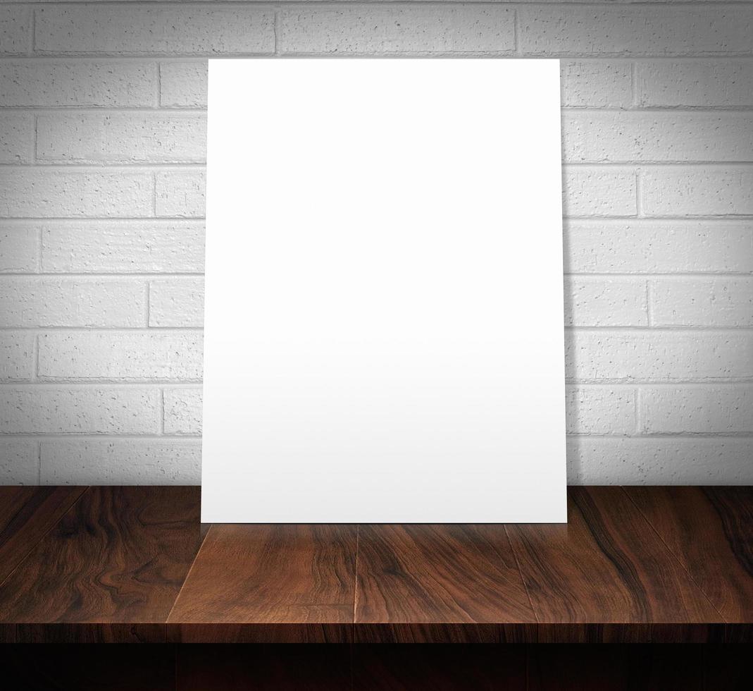 The white poster on a wooden table with a white brick wall photo