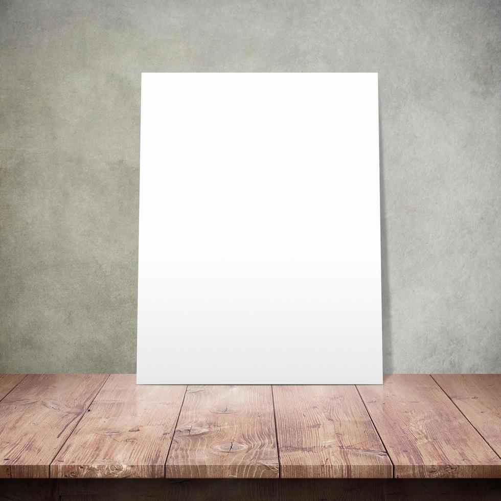 White poster on a wooden table with concrete wall background photo