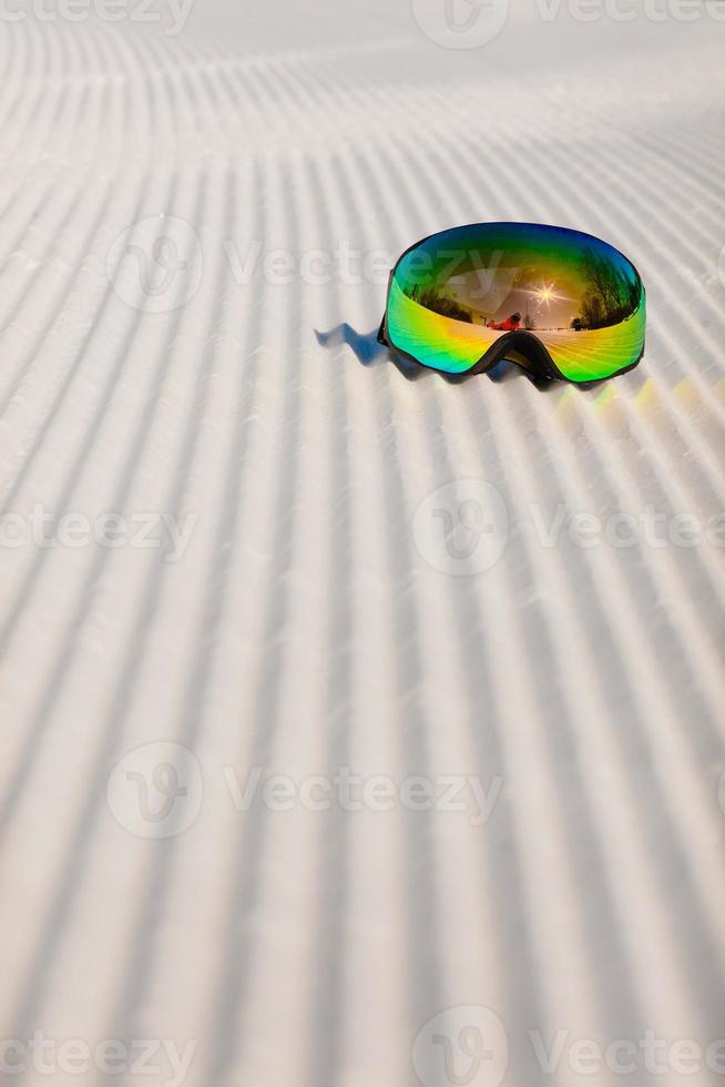 Ski goggles laying on a new groomed snow and empty ski slope photo