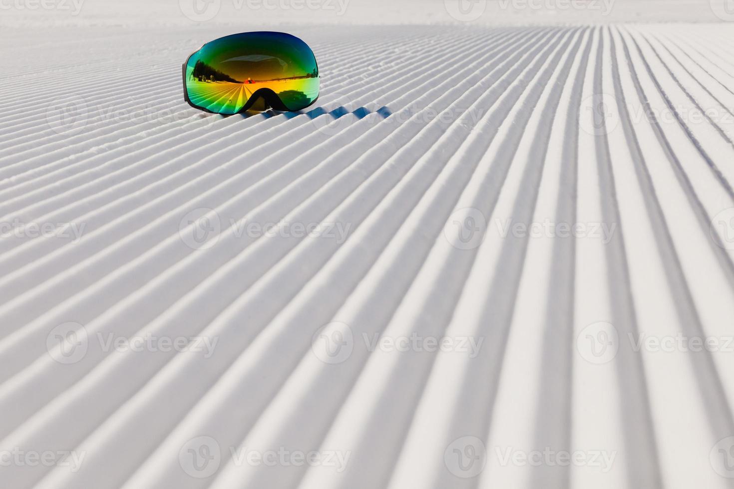 Ski goggles laying on a new groomed snow and empty ski slope photo