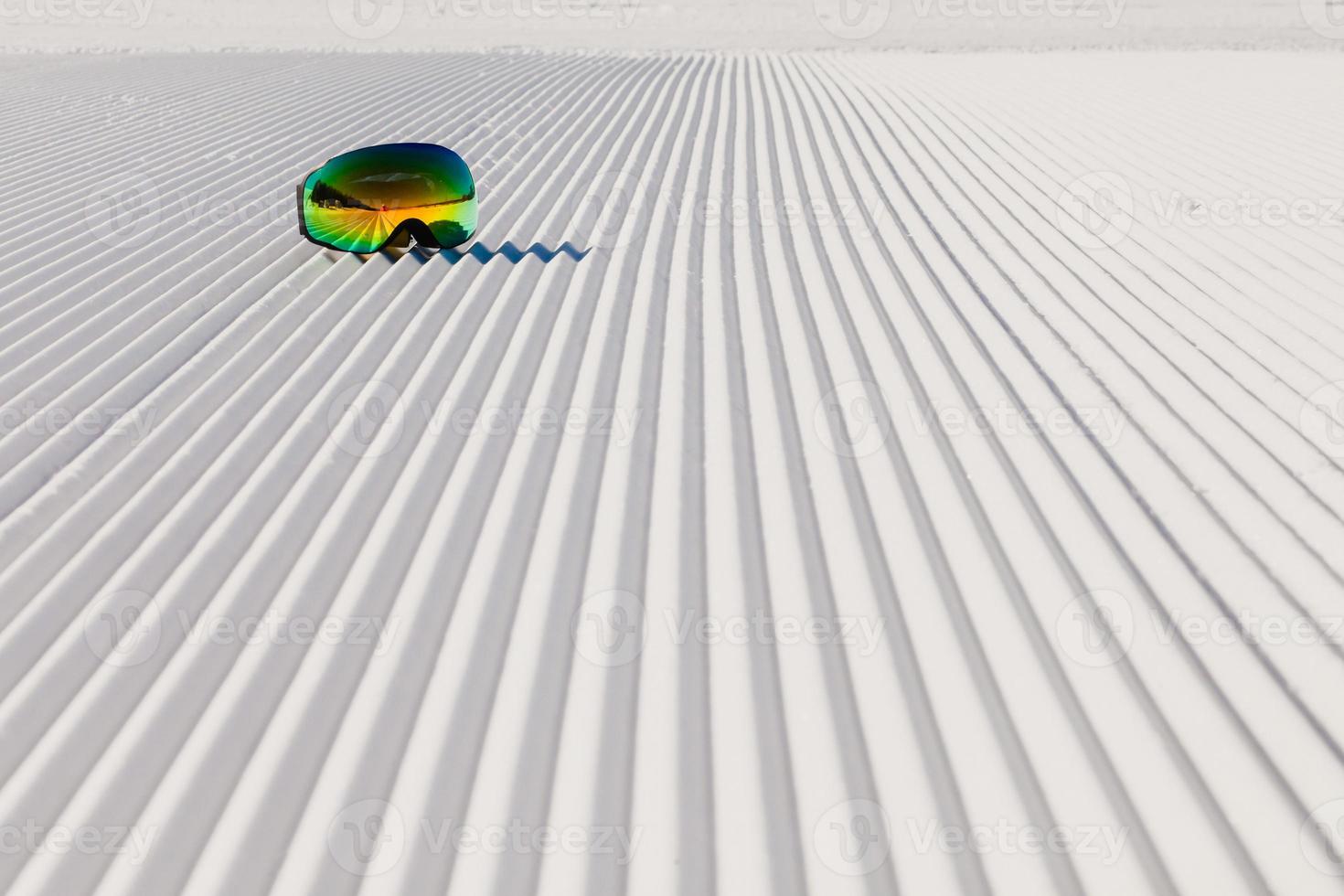 Ski goggles laying on a new groomed snow and empty ski slope photo