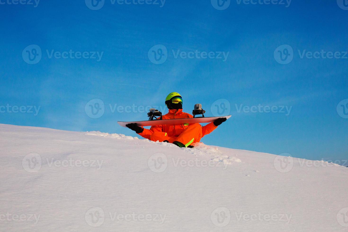 Snowboarder freerider con snowboard blanco sentado en la parte superior de la pista de esquí foto