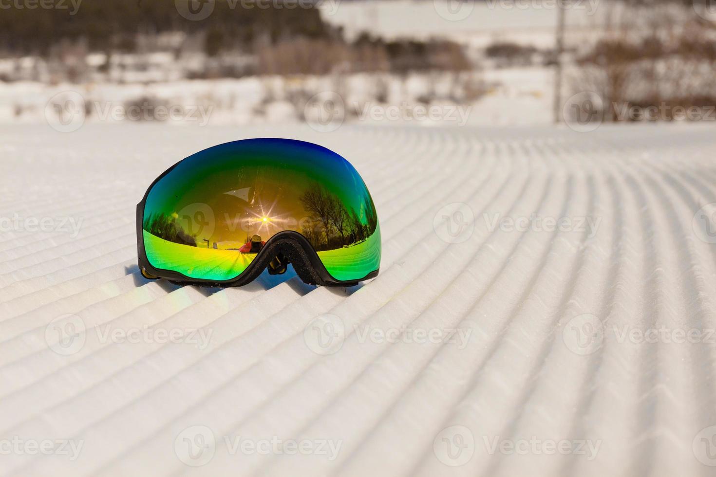 Ski goggles laying on a new groomed snow and empty ski slope photo