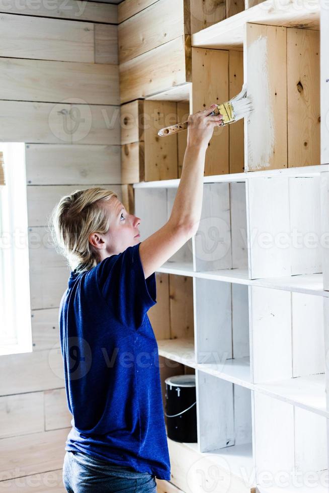 Mujer aplicando la primera capa de pintura en una biblioteca de madera foto