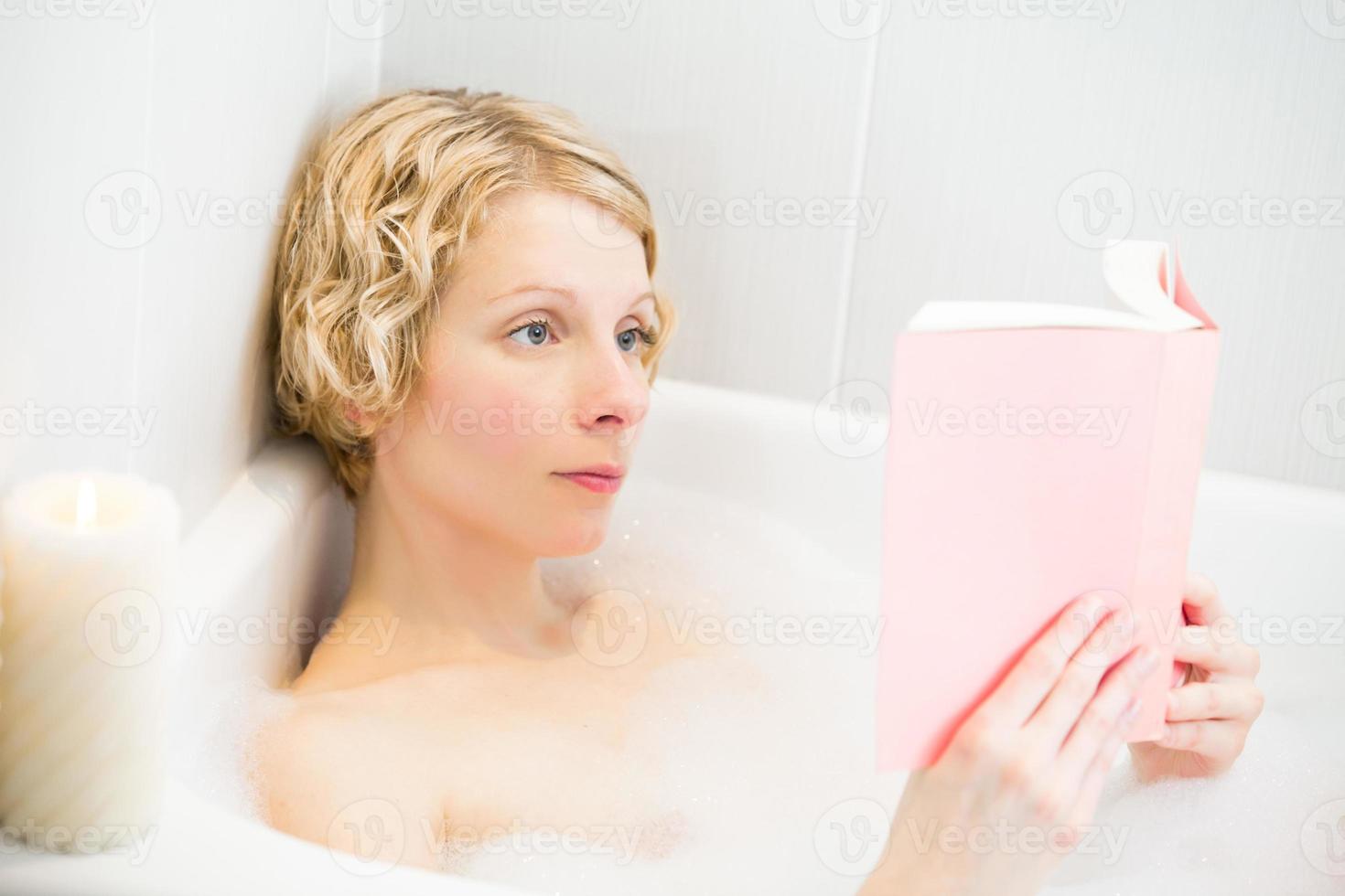Mujer joven relajándose en el baño y leyendo un libro foto