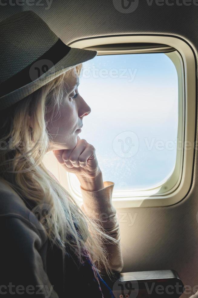 Mujer joven sola mirando afuera y sentado dentro del avión foto