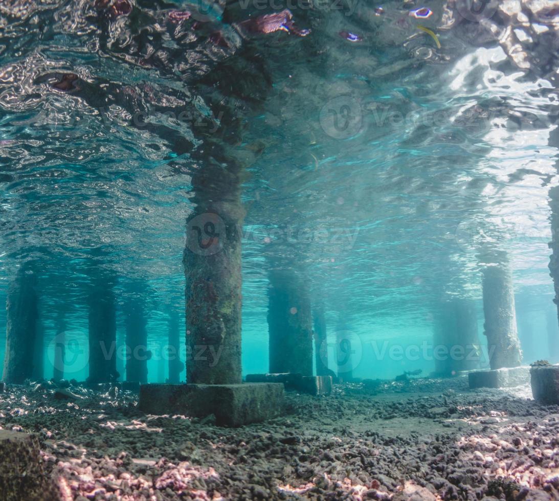 Vista submarina de debajo de un muelle con pilares y luz solar foto