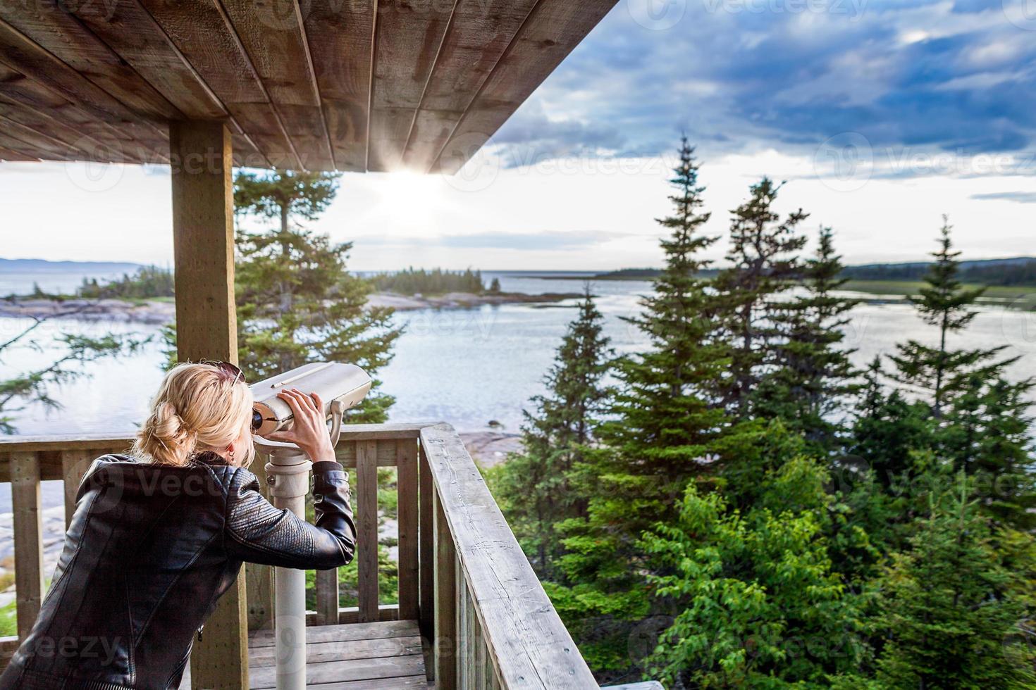 Mujer joven mirando la naturaleza asombrosa a través de un binocular en una torre de observación foto