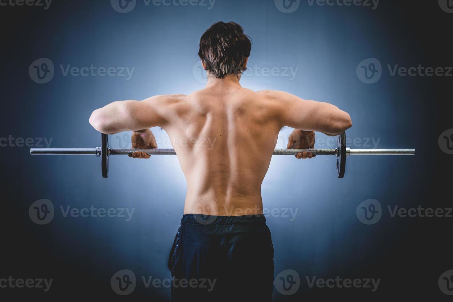 Muscular man doing shoulders exercise with barbell photo